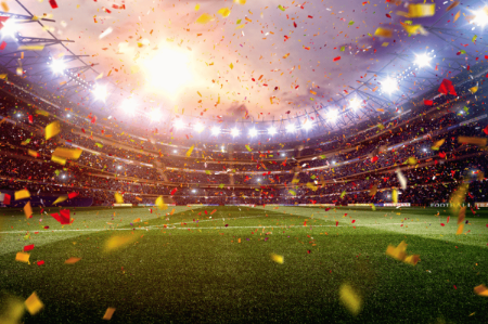 Close shot of soccer stadium field with bright lights above and confetti falling