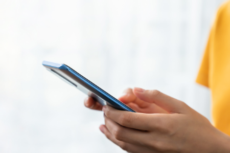 A closeup of a male in yellow shirt holding his mobile phone with two hands while using thumbs to type