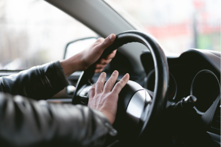 A close shot of a driver inside the car with one hand gripping the steering wheel and the other pressed against the car horn.