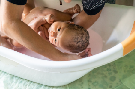 Close shot of a baby in a plastic tub for infants being slowly placed inside by his father's arms. 