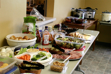 A shot of a folding table crowded with various food set up in containers on top of it.  All of the containers are open and the food is on display.