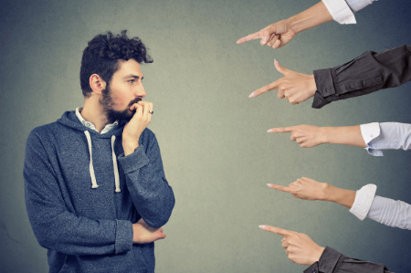 An image of a man standing uncomfortably as five different hands stick into the frame and point at him