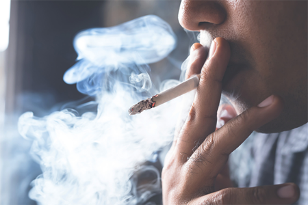 A close shot of a man taking a puff of a cigarette and smoke fills the area all around him